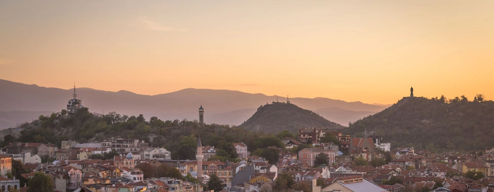 Golden-hour view over the old town of Plovdiv, with a mosque minaret, hills and mountains in the haze